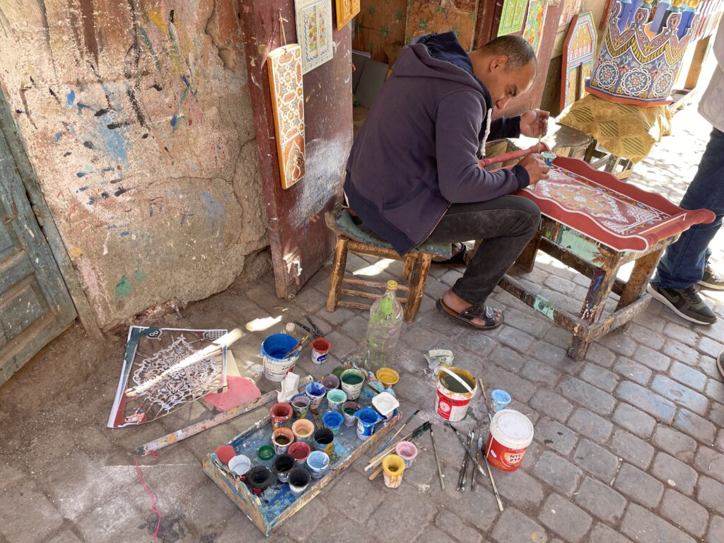 Man painting traditional Moroccan stencil work on a Marrakech artisan tour
